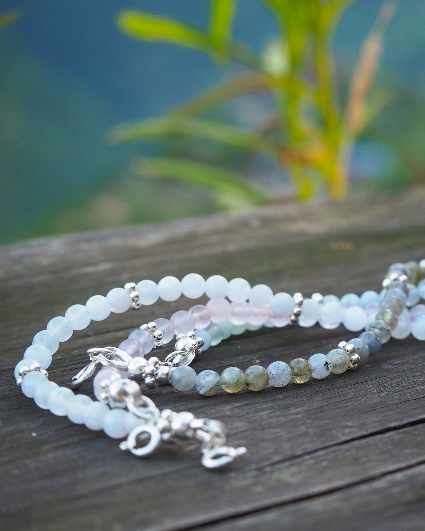 Four handcrafted gemstone bracelets made from aquamarine, moonstone, rose quartz, and labradorite with silver details, placed on a wooden surface - minimalist jewelry by elswre