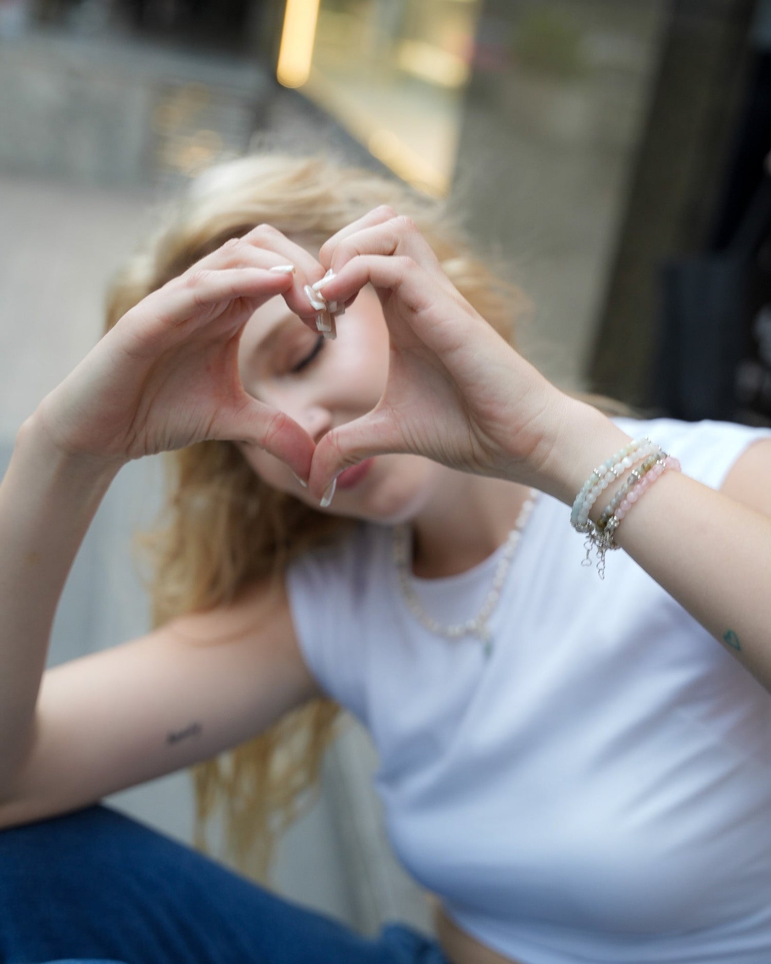 Model forming a heart shape with her hands while wearing layered silver and gemstone bracelets – playful handcrafted jewelry by elswre.