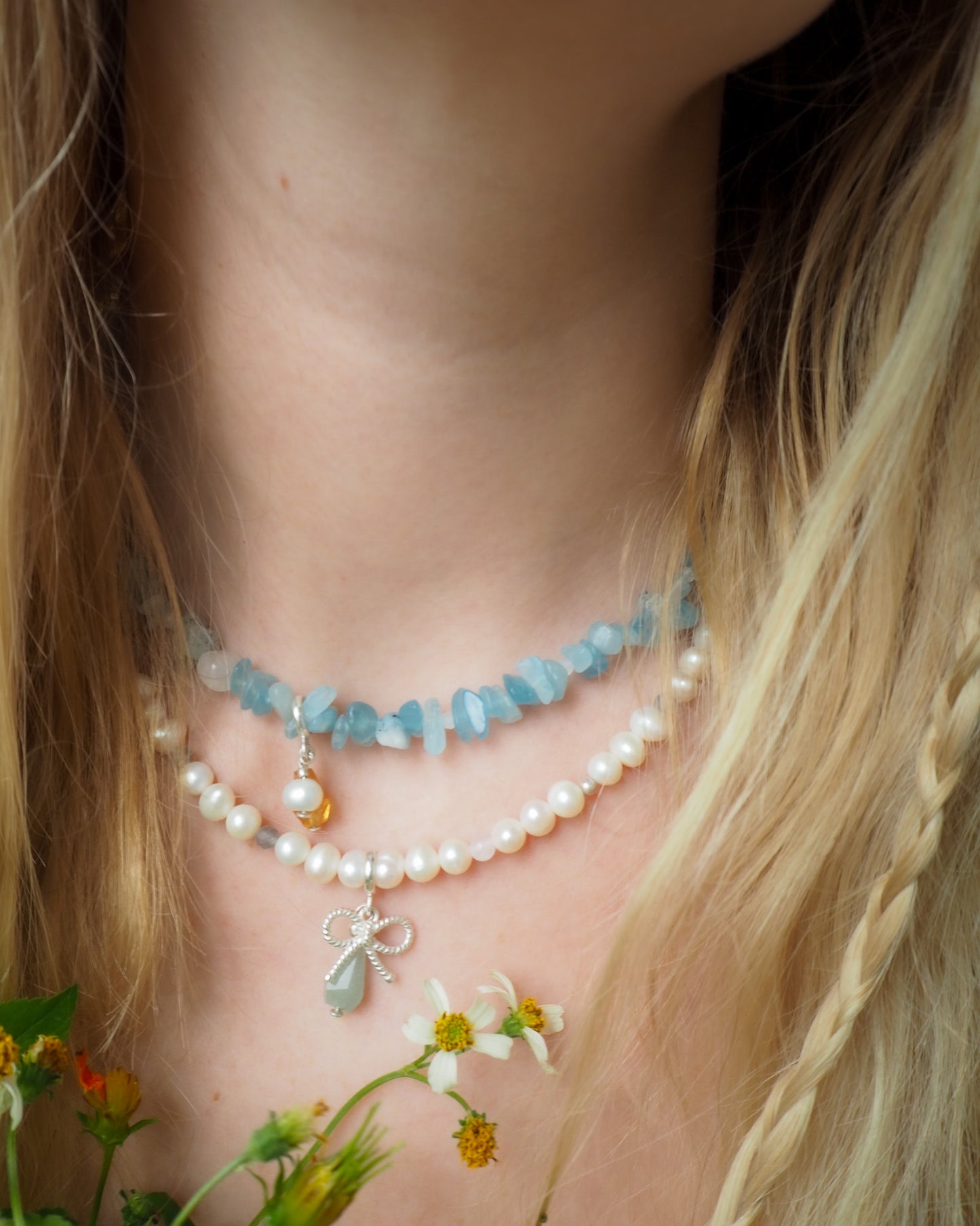 Close-up of pearl necklace with aquamarine and silver bow charms layered on model’s neck – modern handcrafted jewelry from elswre.