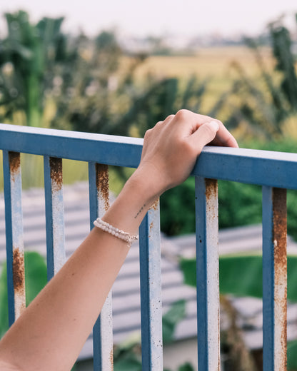 Hand resting on a blue railing, wearing a handcrafted moonstone and silver bracelet - minimalist travel-inspired jewelry by elswre