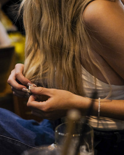 Woman with long blonde hair sitting at a bar, wearing a handcrafted moonstone and silver bracelet - minimalist jewelry by elswre
