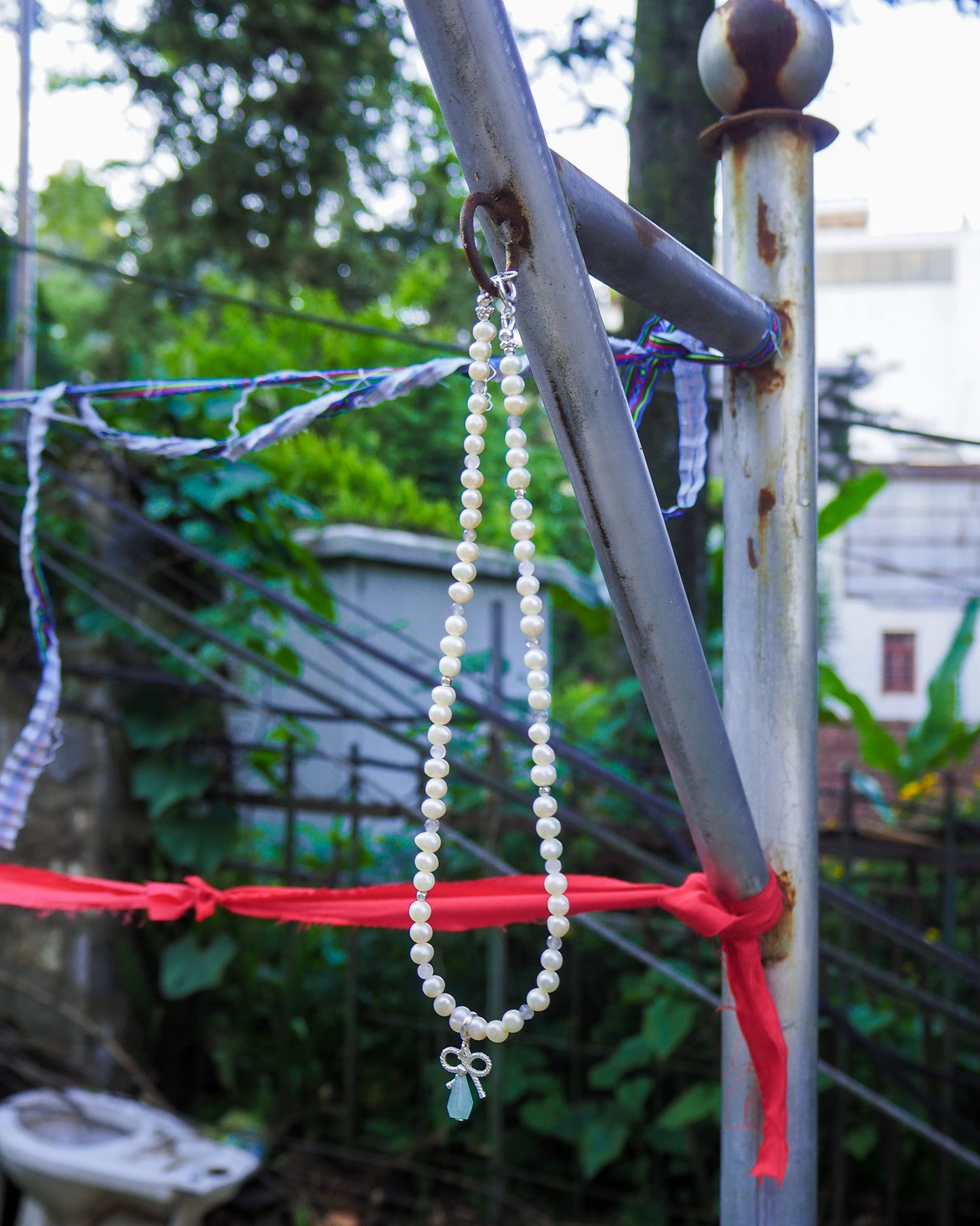 Pearl necklace with aquamarine and silver bow charms hanging among green leaves – natural handcrafted jewelry inspired by Vietnam by elswre.
