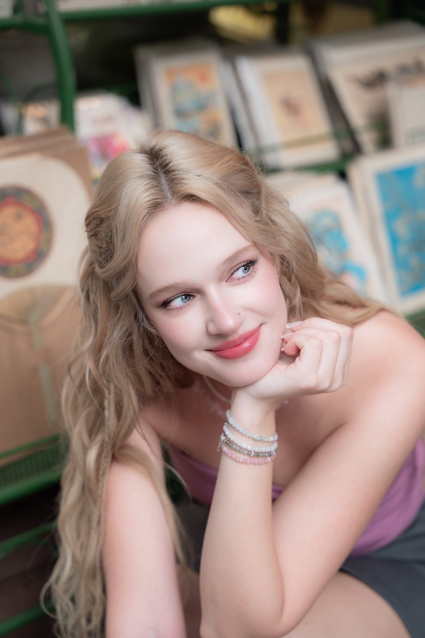 Woman wearing elswre pearl bracelet and gemstone necklace, smiling while sitting outdoors near a market stall in Saigon.