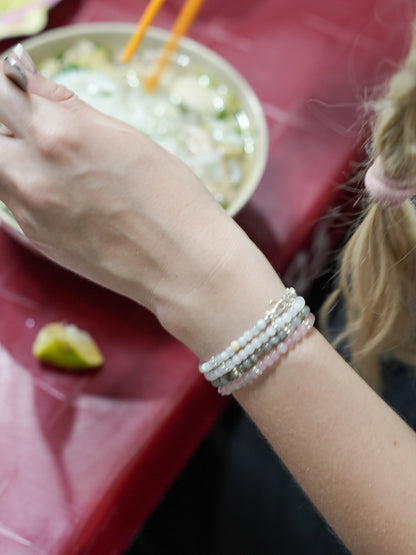 Hand holding chopsticks over a bowl of noodles, wearing layered pearl and gemstone bracelets in silver - travel-inspired jewelry by elswre