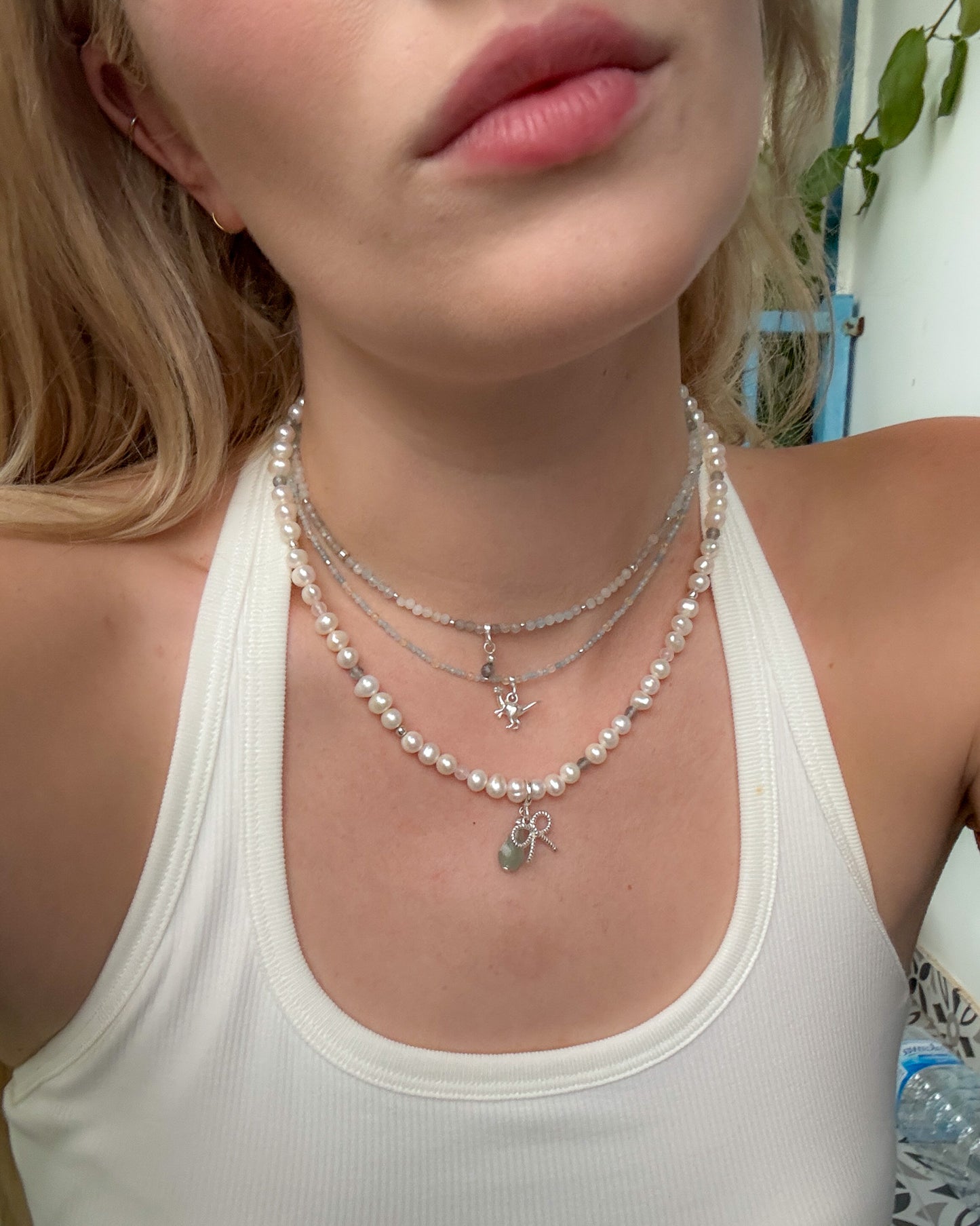 Layered necklaces featuring aquamarine and light citrine beads with a silver dinosaur charm, styled with a pearl necklace and white tank top – travel-inspired jewelry by elswre