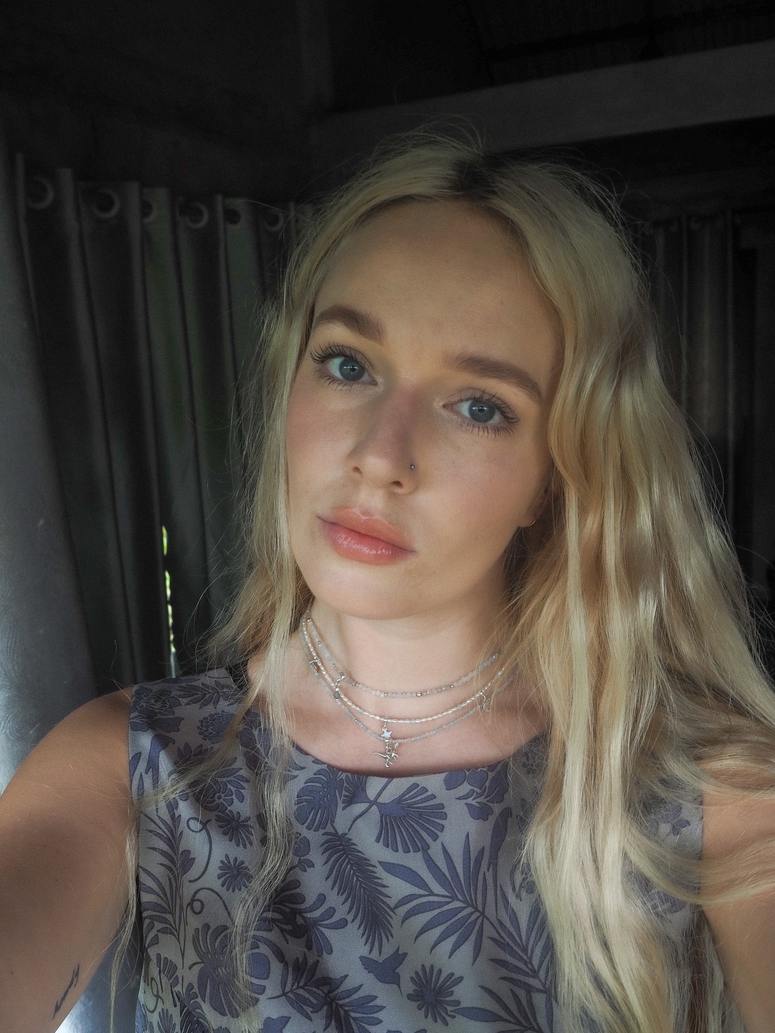 Woman wearing an aquamarine and light citrine beaded necklace with a small silver dinosaur charm – soft natural light portrait for elswre’s travel-inspired jewelry collection