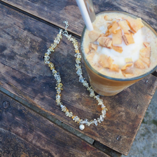 Citrine and silver necklace with pearl charm displayed beside an iced Vietnamese coffee on a wooden table – handmade gemstone jewelry by elswre.