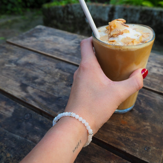 Hand holding an iced coffee while wearing a handcrafted moonstone and silver bracelet - travel-inspired jewelry by elswre