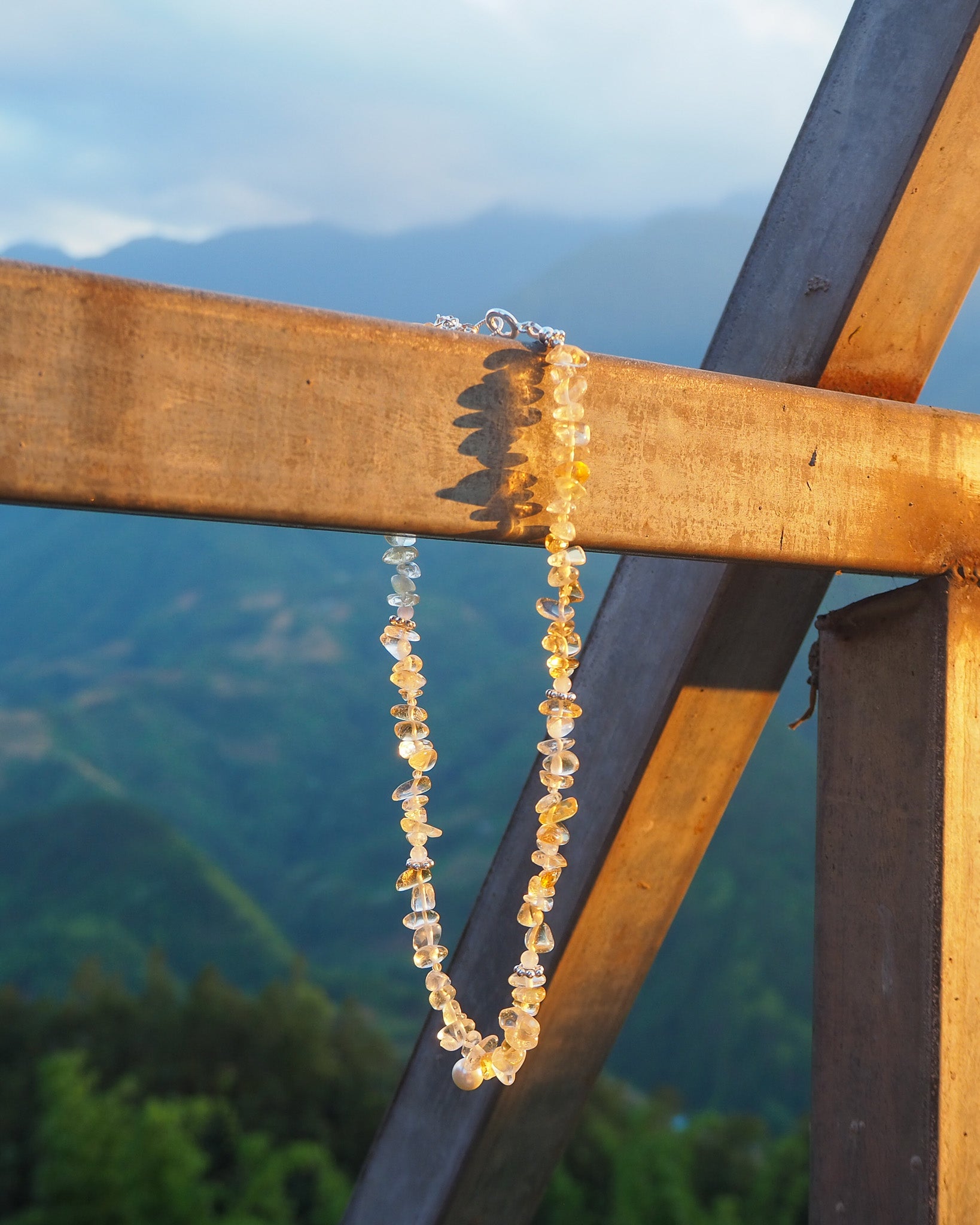 Citrine and silver necklace with pearl pendant hanging on a yellow wooden frame – modern gemstone jewelry inspired by Vietnam by elswre.
