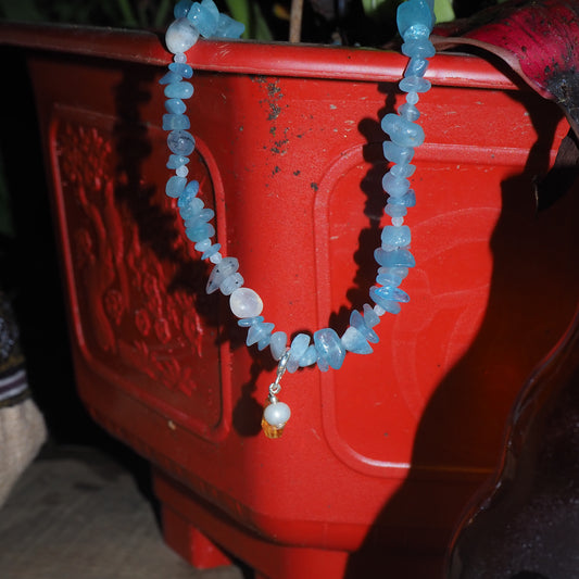 Aquamarine chip necklace with pearl and light citrine charm, displayed on a red planter – travel-inspired jewelry by elswre
