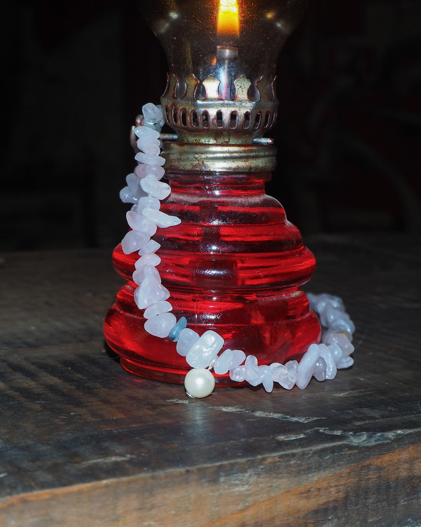 Rose quartz and pearl necklace draped over a vintage red oil lamp – soft pink stones glowing in warm light, photographed for elswre’s Vietnam-inspired collection