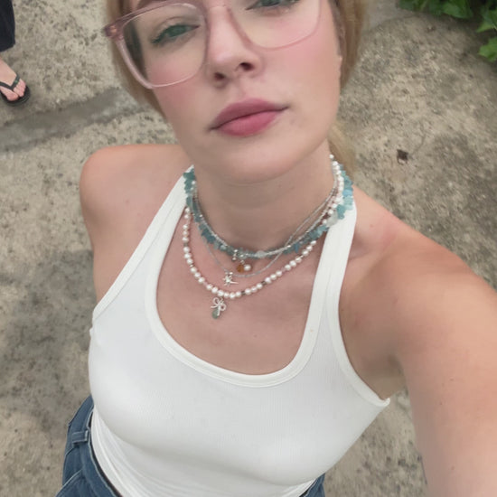 Short video of a pearl necklace with aquamarine and silver bow charms gently moving in natural light – handmade gemstone jewelry by elswre.